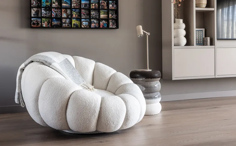 Een moderne zetel met bijzettafel en elegante tafellamp en een open vakkenkast met vazen en sculpturen.