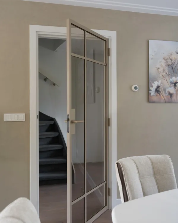 Eetkamer met witte tafel en stoelen en stalen deur naar de hal voor meer daglicht en een ruimtelijk gevoel.