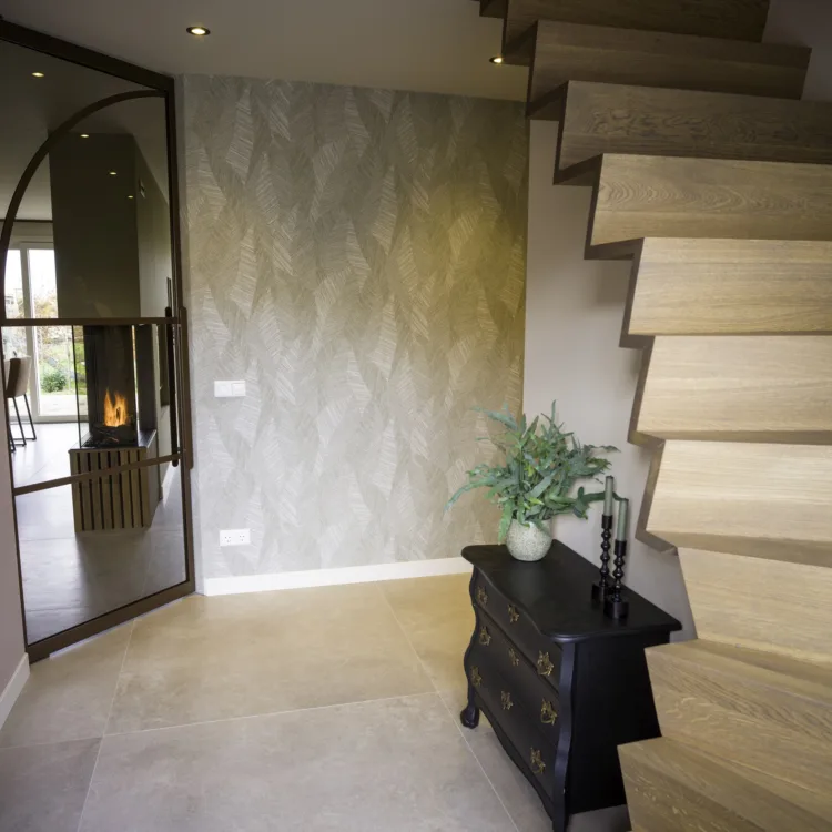 Ruime hal met houten z-trap, lichtgroen behang met natuurlijke print en steenlook tegelvloer